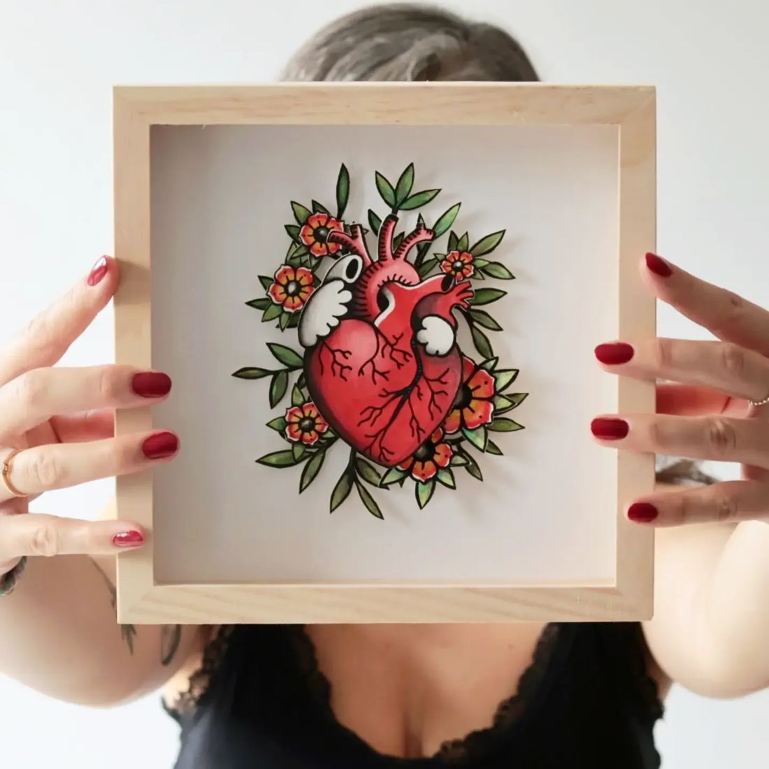Print cœur anatomique fleuri dans un cadre en bois, tenu à deux mains